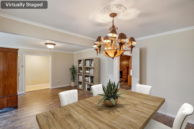 dining room with a brick fireplace, wood-type flooring, ornamental molding, and a chandelier