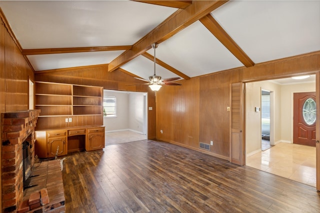 unfurnished living room featuring hardwood / wood-style flooring, lofted ceiling with beams, ceiling fan, and wooden walls