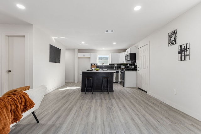 kitchen with a center island, stainless steel appliances, a kitchen breakfast bar, light hardwood / wood-style flooring, and white cabinets