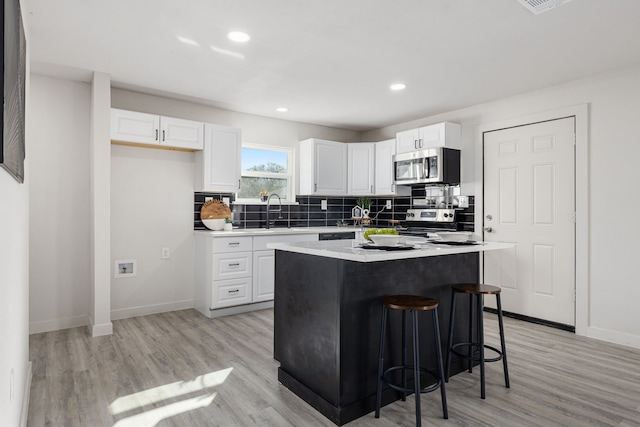 kitchen featuring a kitchen island, light hardwood / wood-style floors, a kitchen bar, white cabinets, and appliances with stainless steel finishes