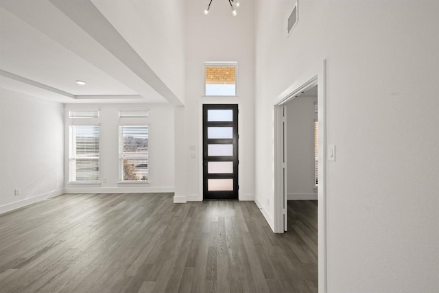 foyer entrance with a raised ceiling, dark hardwood / wood-style floors, a towering ceiling, and a notable chandelier