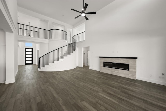 unfurnished living room featuring dark wood-type flooring, a fireplace, a high ceiling, and ceiling fan