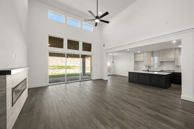 unfurnished living room with dark wood-type flooring, a tiled fireplace, ceiling fan with notable chandelier, and a high ceiling