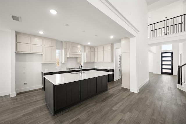 kitchen with white cabinetry, an island with sink, dark wood-type flooring, custom range hood, and sink