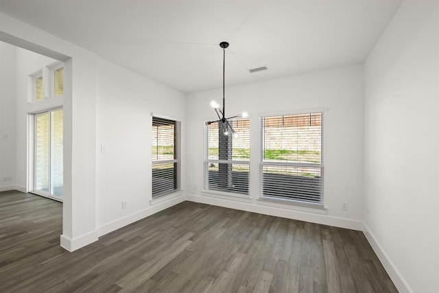 unfurnished dining area with a healthy amount of sunlight, dark hardwood / wood-style floors, and an inviting chandelier