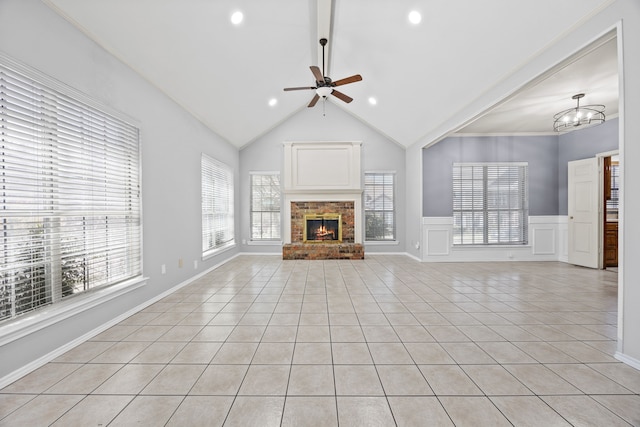 unfurnished living room featuring light tile patterned floors, a wainscoted wall, a brick fireplace, a decorative wall, and ceiling fan with notable chandelier