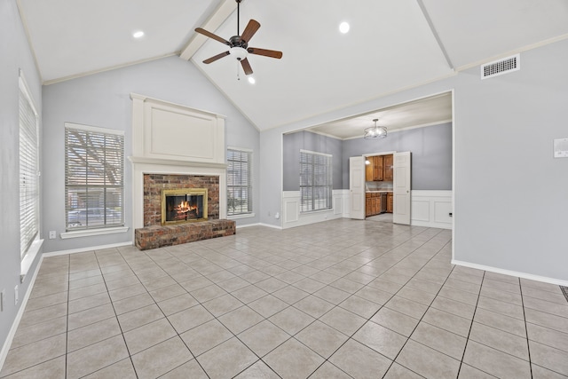 unfurnished living room with beamed ceiling, visible vents, ceiling fan, wainscoting, and a brick fireplace