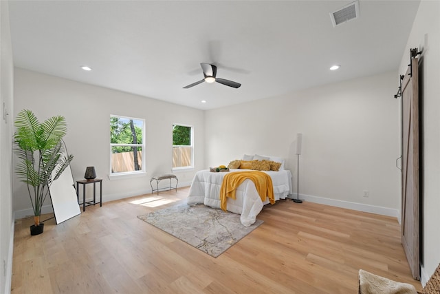 bedroom with a barn door, light hardwood / wood-style floors, and ceiling fan