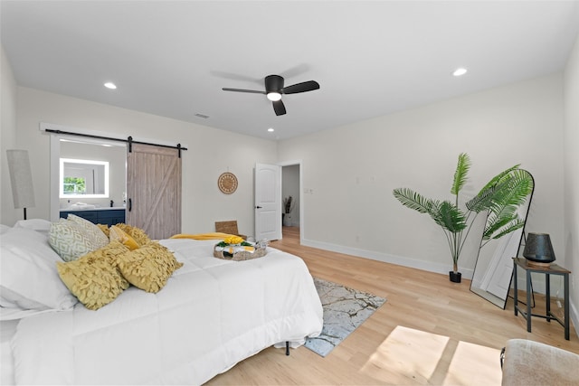 bedroom with ceiling fan, a barn door, and light hardwood / wood-style floors