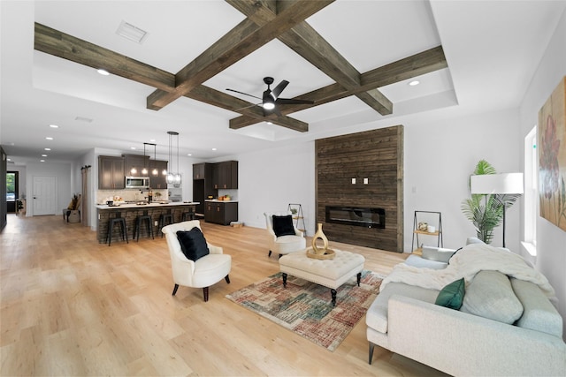 living room with ceiling fan, a large fireplace, coffered ceiling, and light wood-type flooring