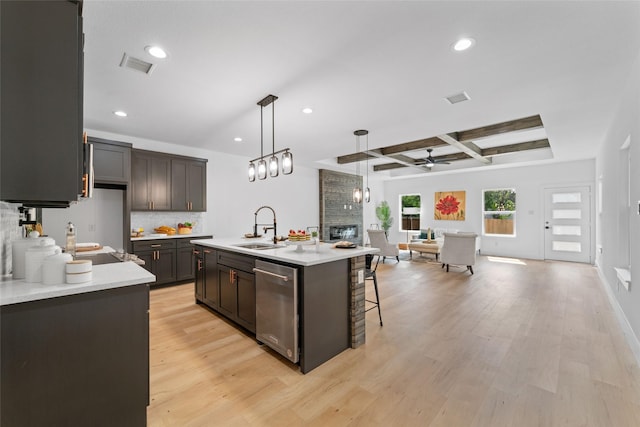 kitchen with pendant lighting, a fireplace, dishwasher, sink, and a kitchen island with sink