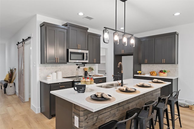 kitchen with sink, stainless steel appliances, a barn door, light hardwood / wood-style floors, and a kitchen island with sink