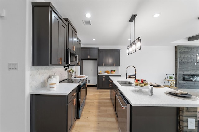 kitchen featuring backsplash, stainless steel appliances, light hardwood / wood-style flooring, and a kitchen island with sink