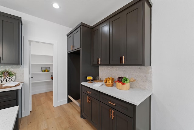 kitchen featuring light stone countertops, light wood-type flooring, and backsplash