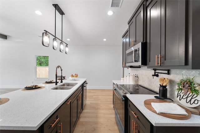 kitchen featuring a kitchen island with sink, light stone countertops, stainless steel appliances, and hanging light fixtures