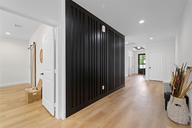 corridor with a barn door and light hardwood / wood-style floors