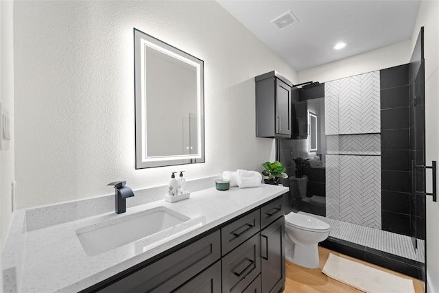 bathroom featuring a tile shower, vanity, hardwood / wood-style flooring, and toilet