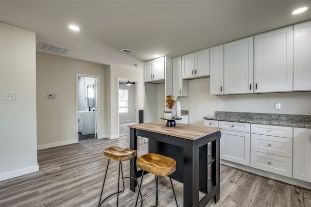 kitchen featuring white cabinets, light hardwood / wood-style flooring, light stone countertops, and ceiling fan