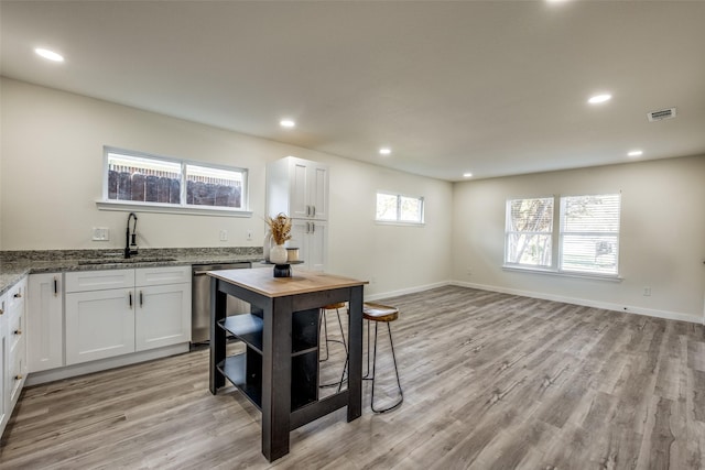 kitchen with light stone counters, white cabinetry, sink, and light hardwood / wood-style flooring