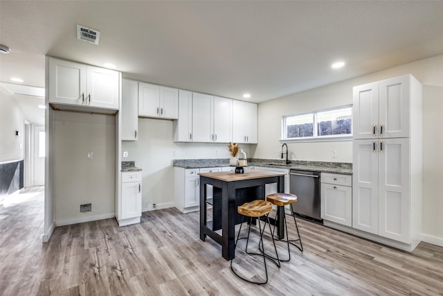 kitchen featuring light stone countertops, white cabinetry, sink, stainless steel dishwasher, and light wood-type flooring