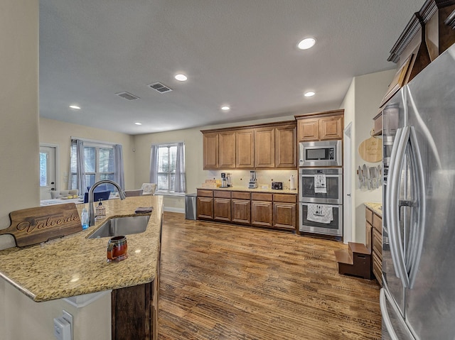 kitchen featuring sink, appliances with stainless steel finishes, dark hardwood / wood-style floors, light stone countertops, and a textured ceiling