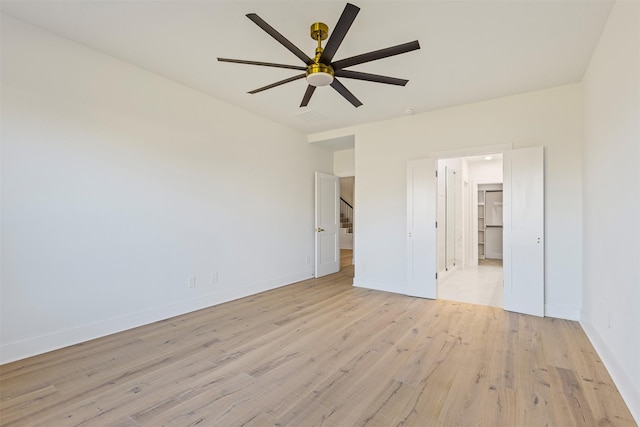 unfurnished bedroom featuring light wood-type flooring, a spacious closet, and ceiling fan