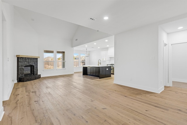 unfurnished living room featuring a fireplace, light wood-type flooring, high vaulted ceiling, and sink