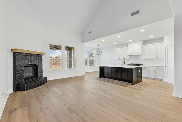 kitchen featuring white cabinetry, high vaulted ceiling, an island with sink, custom range hood, and light wood-type flooring