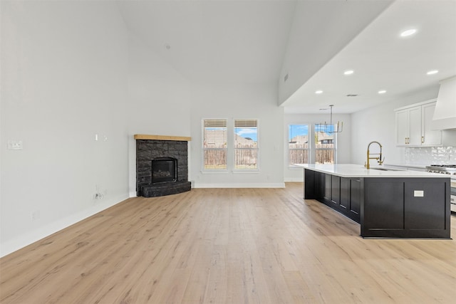 kitchen with a kitchen island with sink, white cabinets, sink, high end stainless steel range, and light hardwood / wood-style flooring