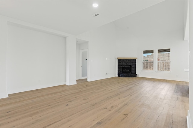 unfurnished living room featuring a stone fireplace, high vaulted ceiling, and light wood-type flooring