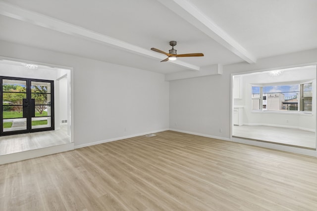 unfurnished living room with plenty of natural light, light wood-type flooring, beam ceiling, and french doors