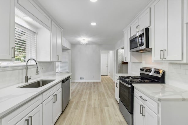 kitchen with sink, stainless steel appliances, white cabinets, and light stone countertops