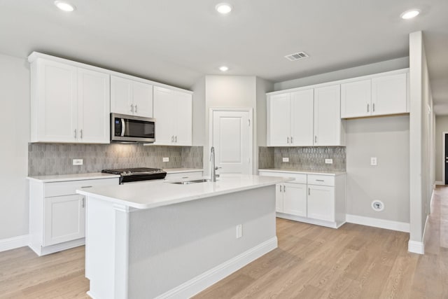 kitchen with white cabinets, appliances with stainless steel finishes, a kitchen island with sink, and sink