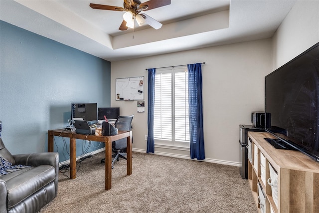 office featuring a raised ceiling, ceiling fan, and light colored carpet