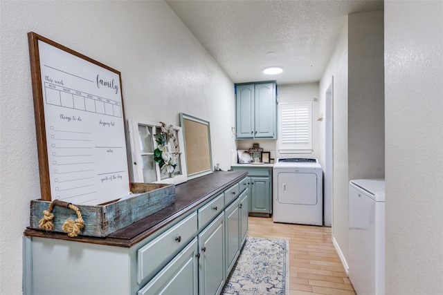 laundry area with cabinets, a textured ceiling, light hardwood / wood-style flooring, and washing machine and clothes dryer