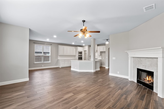 unfurnished living room with sink, dark hardwood / wood-style floors, ceiling fan, and a tiled fireplace