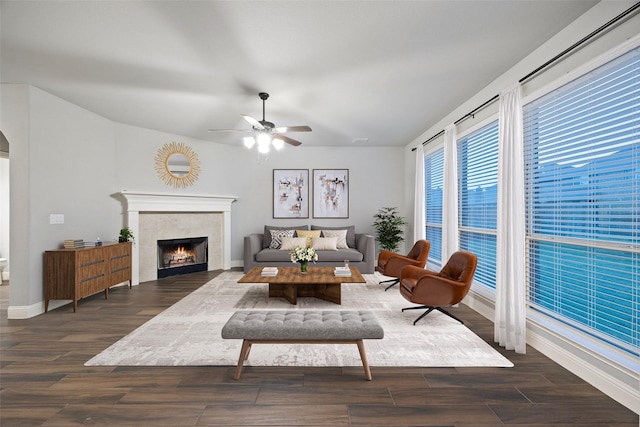 living room featuring a fireplace, ceiling fan, and dark wood-type flooring