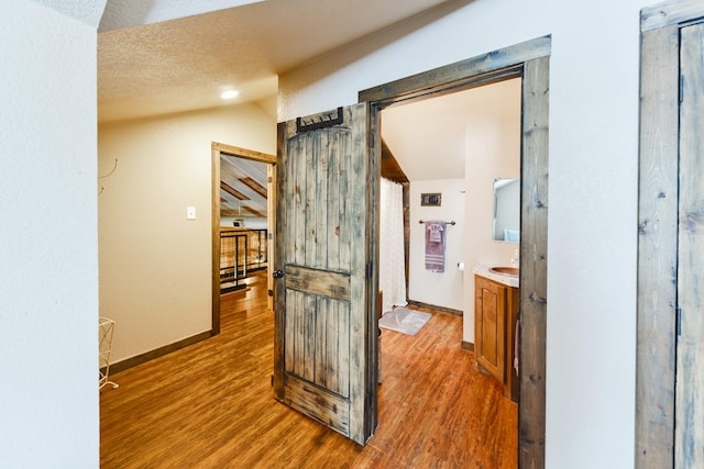 hallway featuring a textured ceiling, a barn door, wood-type flooring, and lofted ceiling