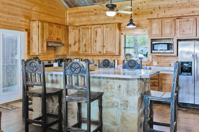 kitchen with pendant lighting, lofted ceiling, a kitchen breakfast bar, wooden walls, and appliances with stainless steel finishes