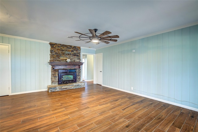 unfurnished living room with ceiling fan, a stone fireplace, crown molding, hardwood / wood-style floors, and wooden walls