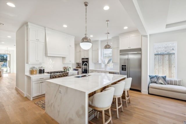 kitchen featuring premium range hood, white cabinetry, a center island with sink, and stainless steel appliances