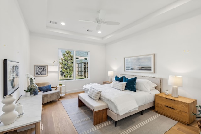 bedroom with ceiling fan, light wood-type flooring, and a tray ceiling