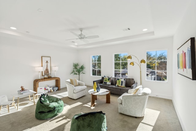 carpeted living room with ceiling fan and a raised ceiling