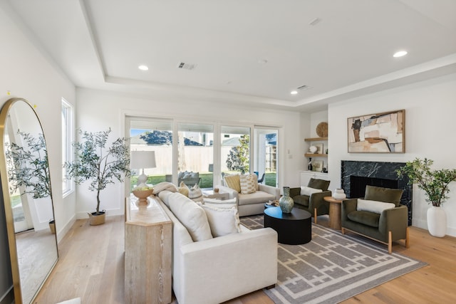 living room with a tray ceiling, light hardwood / wood-style flooring, and a high end fireplace