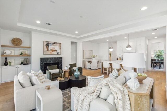 living room featuring light wood-type flooring, a raised ceiling, and a premium fireplace