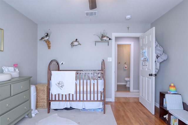 bedroom featuring a nursery area, ceiling fan, connected bathroom, and light hardwood / wood-style flooring