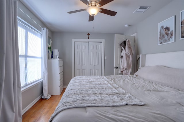 bedroom with multiple windows, light hardwood / wood-style flooring, ceiling fan, and a closet