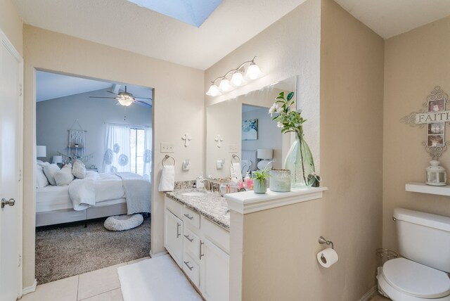 bathroom featuring ceiling fan, tile patterned flooring, vaulted ceiling with skylight, vanity, and toilet