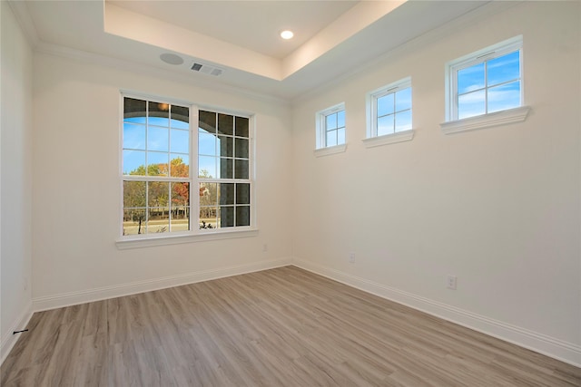 empty room with crown molding, a raised ceiling, and light hardwood / wood-style flooring