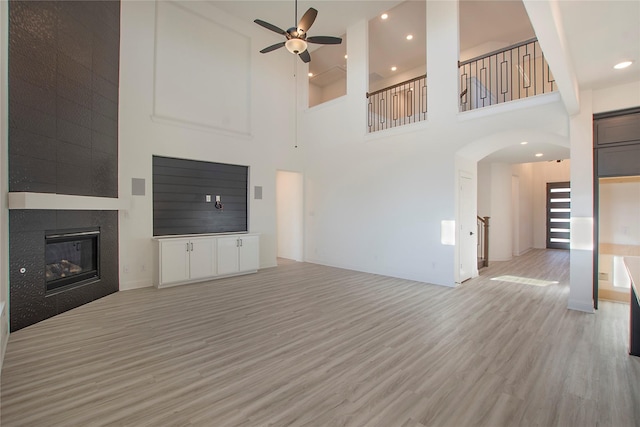 unfurnished living room with ceiling fan, a tile fireplace, and light wood-type flooring